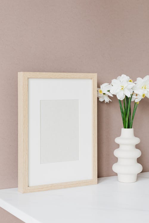 Empty Picture Frame Standing Next to Vase of Flowers