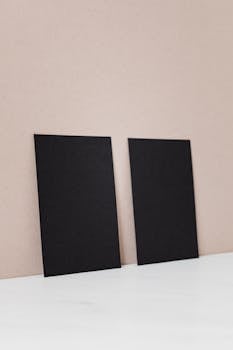 Two black business cards propped against a beige wall, perfect for mockups.