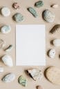 Top view composition of assorted whole and cracked pebbles arranged around white empty paper sheet on beige surface