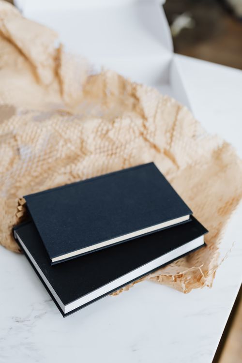 Free From above of notebook pair with black empty hardcover placed with packing paper and white cardboard box on white marble table Stock Photo