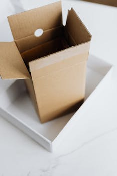 Open cardboard box placed inside a larger white box on marble table, perfect for delivery and storage themes.