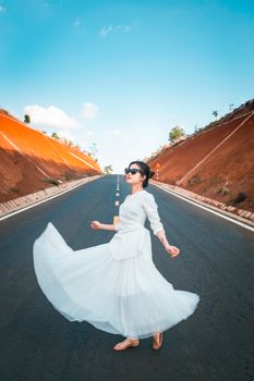 一位身着时髦白色连衣裙的女子，在开阔的道路上旋转，以清澈的蓝天为背景，拥抱自由与欢乐