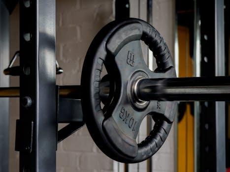 Close-up image of a barbell with a 10kg weight plate in a gym setting, emphasizing strength training equipment.