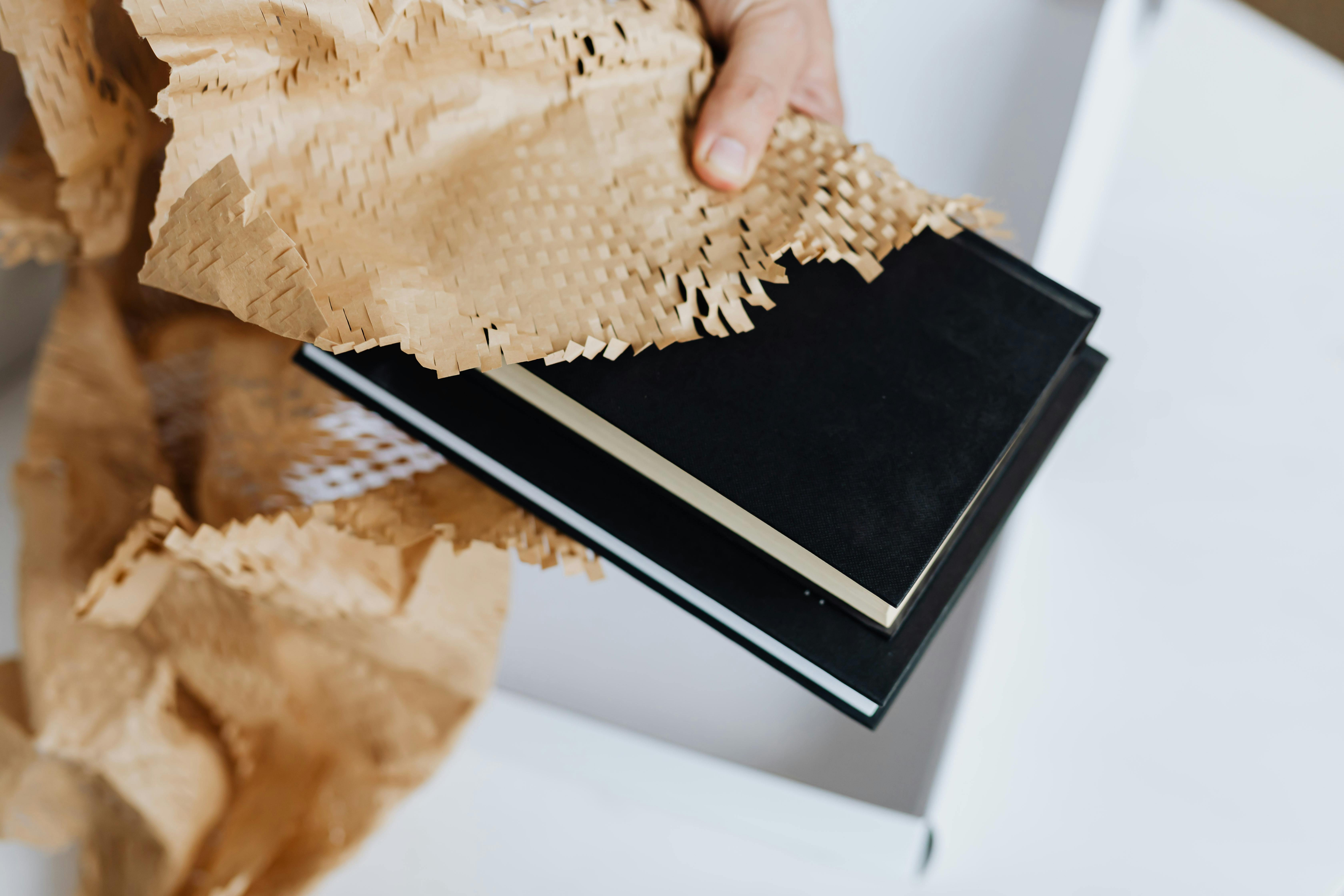 crop man arranging packing paper on notebooks for sending