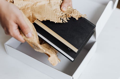 Anonymous man wrapping pair of black notebooks in packing paper