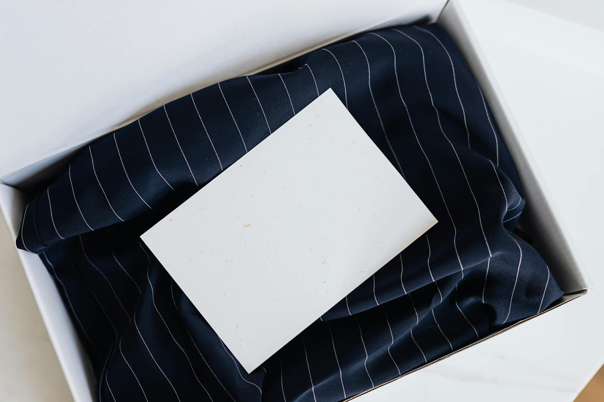 A blank card resting on elegant pinstripe fabric in a gift box.