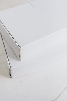 Simple white cardboard boxes stacked on a light marble surface, ideal for packaging mockups.