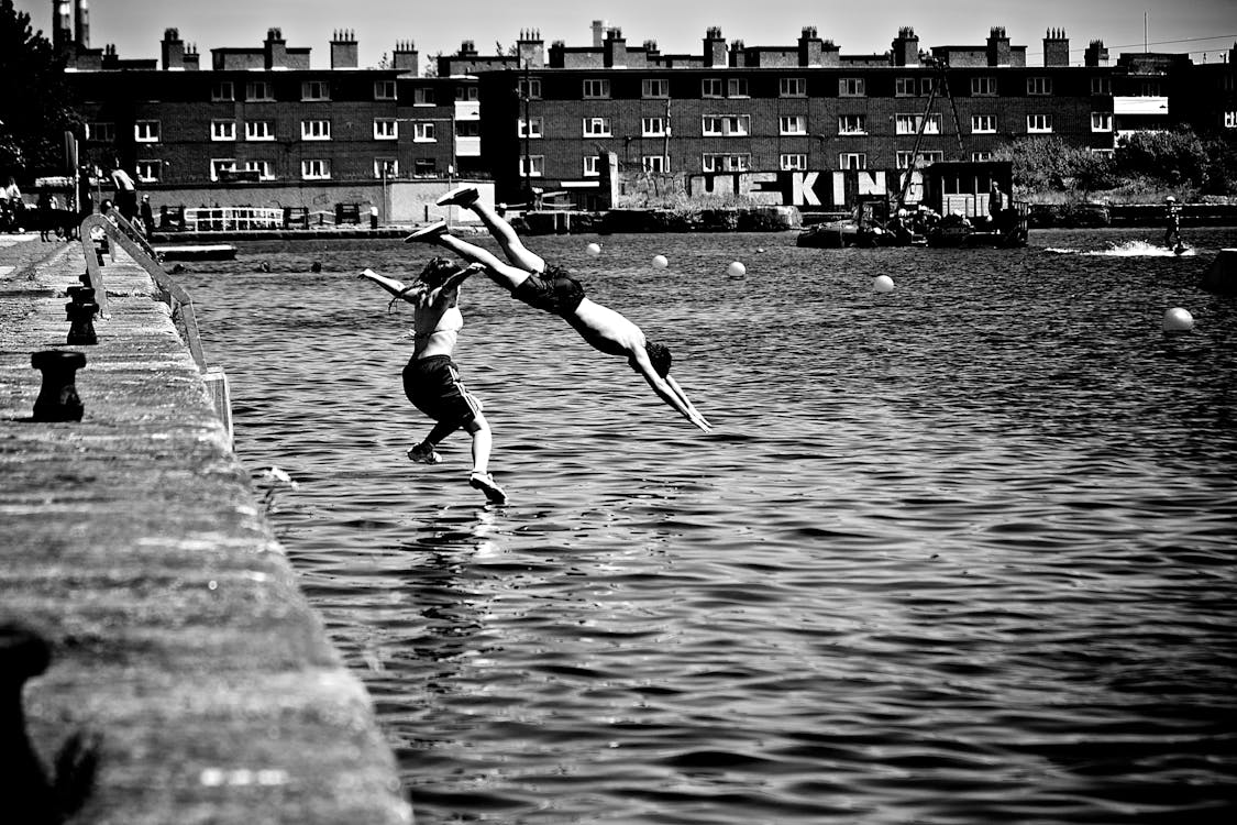 Free Boy and Girl Jumping in Body of Water Stock Photo