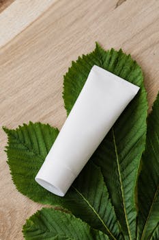 White cosmetic tube on lush green leaves promoting natural skincare.
