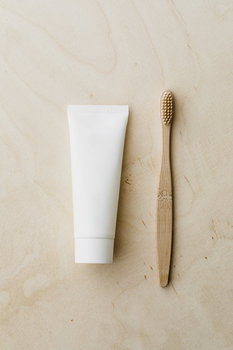 White Toothpaste Tube And Bamboo Toothbrush On Wooden Surface