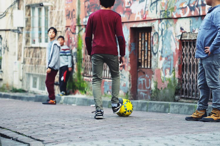 A Young Man In Red Sweater And Blue Denim Jeans Playing Soccer