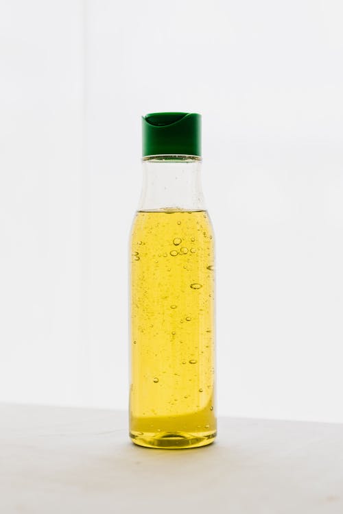 Yellow body oil with bubbles in transparent plastic bottle with green cap on table against white background