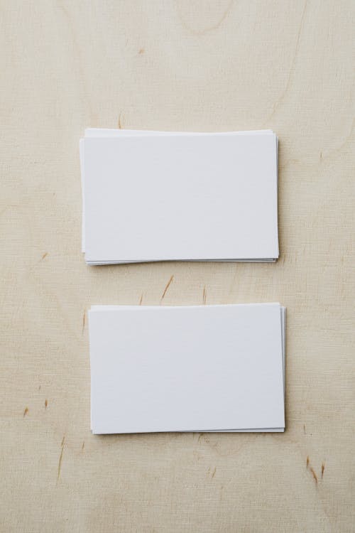 Top view of stacks of white mockup greeting cards placed on light wooden desk in soft daylight