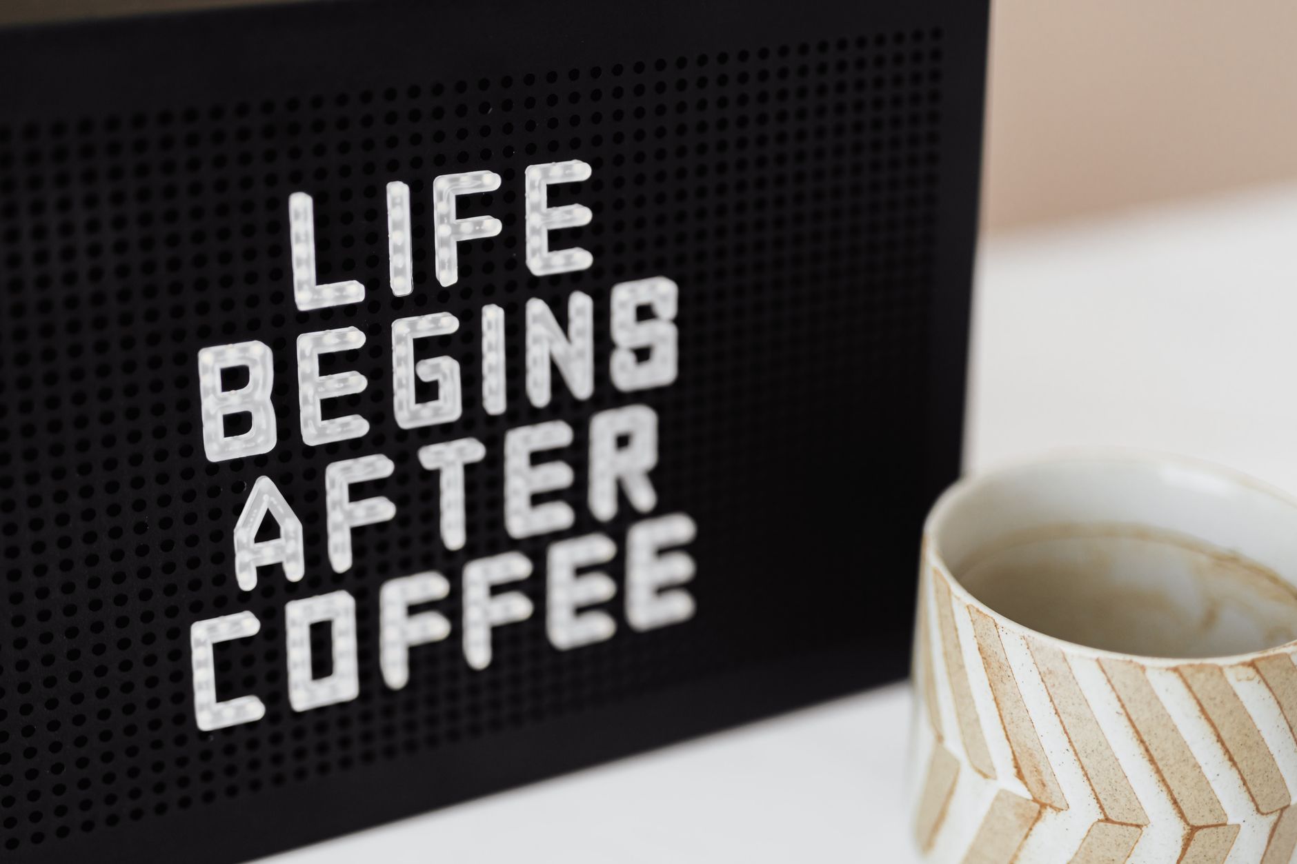 Peg message board with Life Begins After Coffee motto and empty ceramic cup of coffee with creative striped design on white table