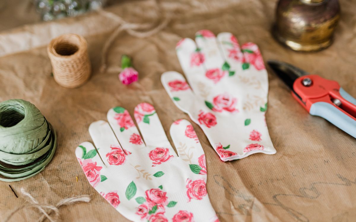 From above of pair of white garden gloves with floral pattern on brown craft paper together with floral cutter and twine in flower shop
