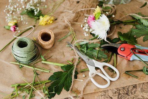 Free From above of scissors and pruners together with twine rolls and big mess of cut leaves and separate flowers on brown paper in flower shop Stock Photo