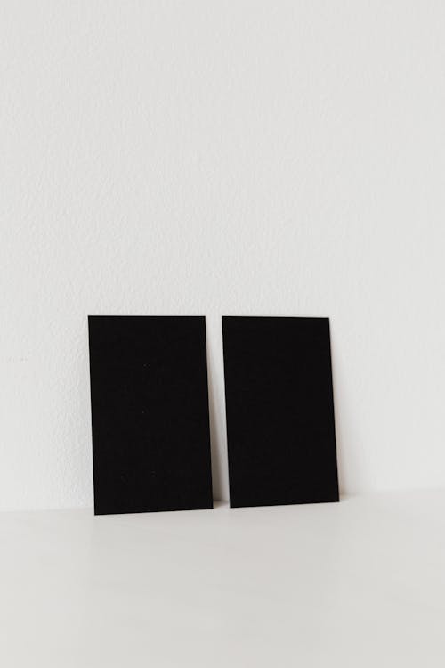 Pair of black business cards with no text leaning on white wall in studio