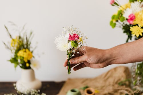 Free Crop faceless male florist arranging little bouquet of white chrysanthemums and pink carnations decorated with gypsophila in flower shop Stock Photo