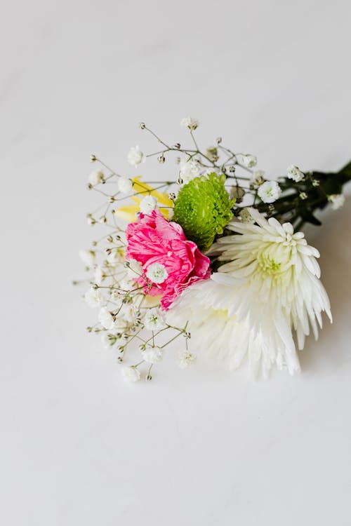Free From above of small bouquet of beautifully arranged white and green chrysanthemums and pink carnation complemented with baby breaths placed on white marble table Stock Photo