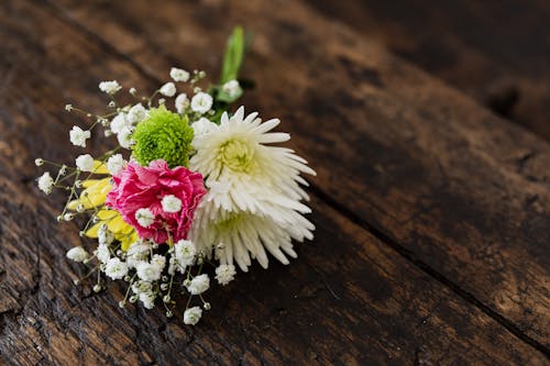 From above of elegant bouquet of differently colored chrysanthemums with pink carnation and tender Gypsophila on contrasting dark brown rustic bench
