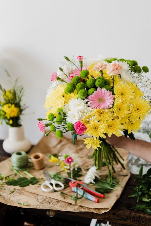 Crop unrecognizable florist composing chrysanthemum bouquet in workshop near messy table covered with cut leaves and floristry tools