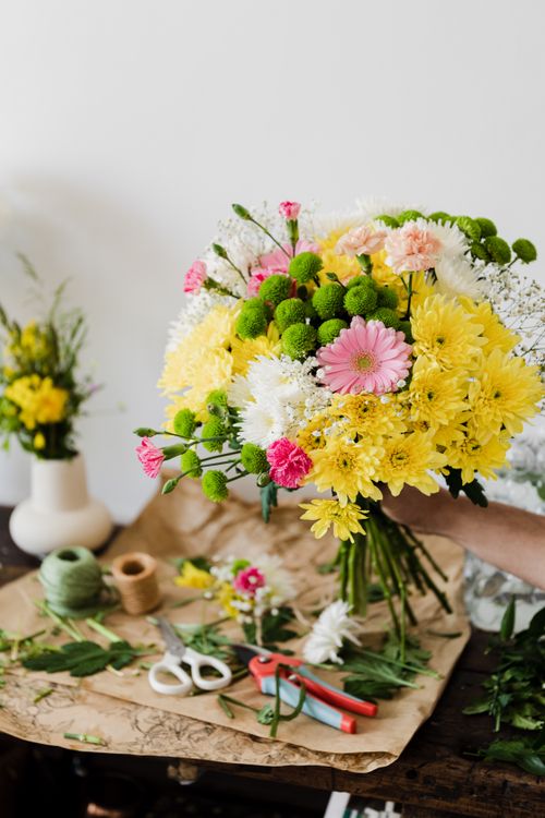 Free Crop unrecognizable florist composing chrysanthemum bouquet in workshop near messy table covered with cut leaves and floristry tools Stock Photo