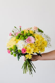 Vibrant bouquet with yellow, pink, and white flowers held against a white backdrop.