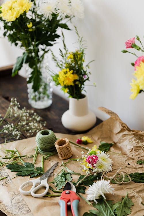 Free Scissors and pruner together with twine rolls among cut leaves and flowers on wooden table with vase bouquets in floristry workshop Stock Photo