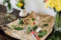 Scissors and pruner on craft paper covered with cut leaves and flowers among bouquets on wooden table in floristry workshop