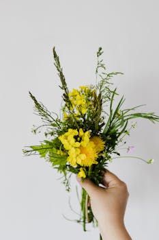 A vibrant bouquet of yellow wildflowers held against a plain background.