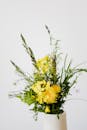 白色花瓶里点缀着黄色花朵的明亮野花花束，背景衬托着浅色