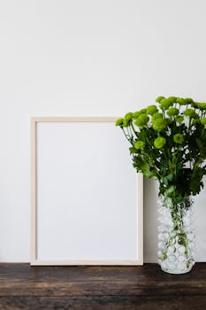 深棕色木桌上，时尚玻璃花瓶中的绿色菊花花束与空的木框实物图片