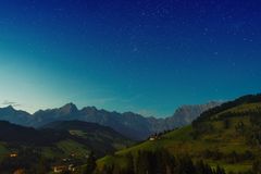 Picturesque green grassy hills located against cloudless starry sky in evening in countryside