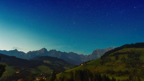 Picturesque green grassy hills located against cloudless starry sky in evening in countryside