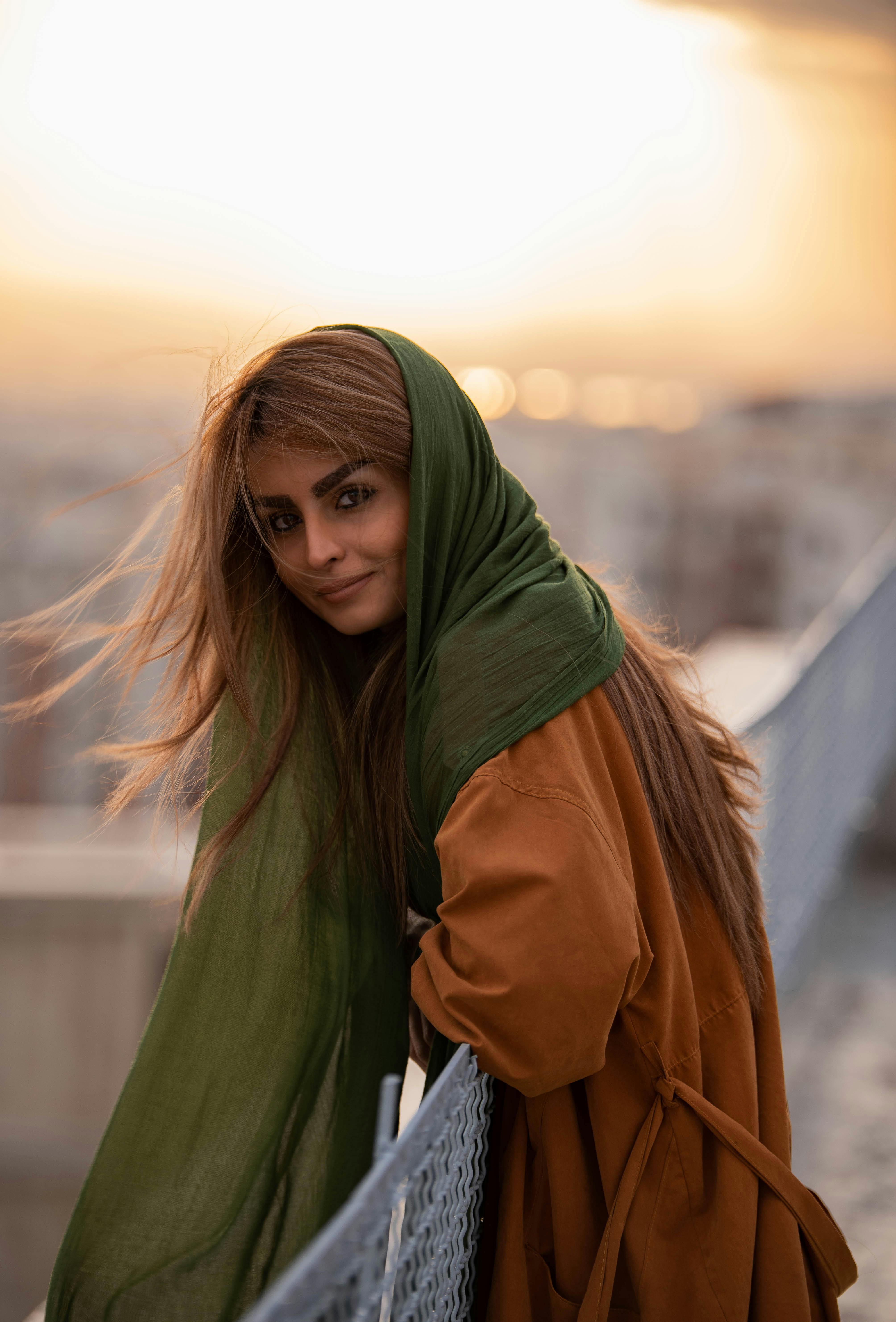 A beautiful woman smiles wearing a green scarf outdoors at sunset.