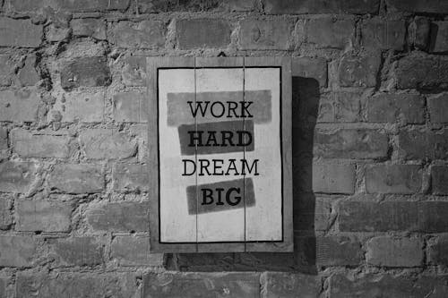 Black and white frame with inspirational Work Hard Dream Big inscription hanging on brick wall