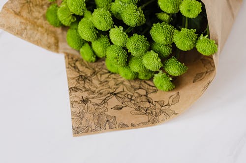 Bouquet of craspedia wrapped in flower paper packaging and placed on white surface