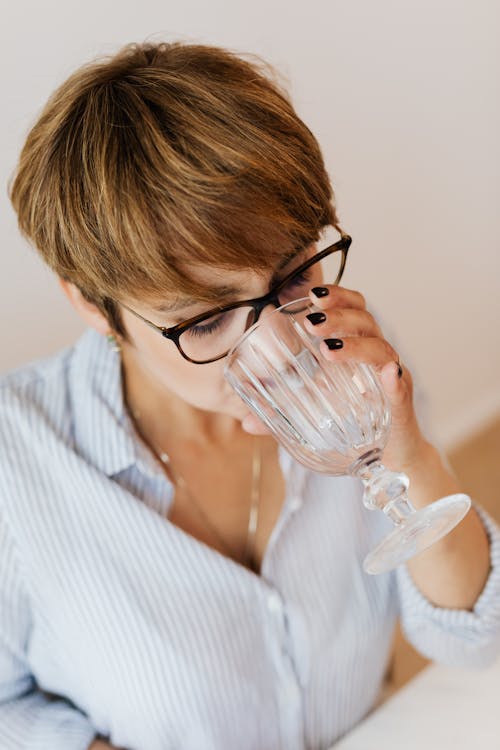Free From above of female with short hair in eyeglasses and shirt with stripes drinking while sitting at white table Stock Photo