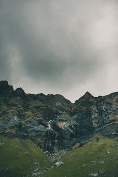 在乡村灰色多云的天空下，瀑布从粗糙的山脉低角度倾泻而下