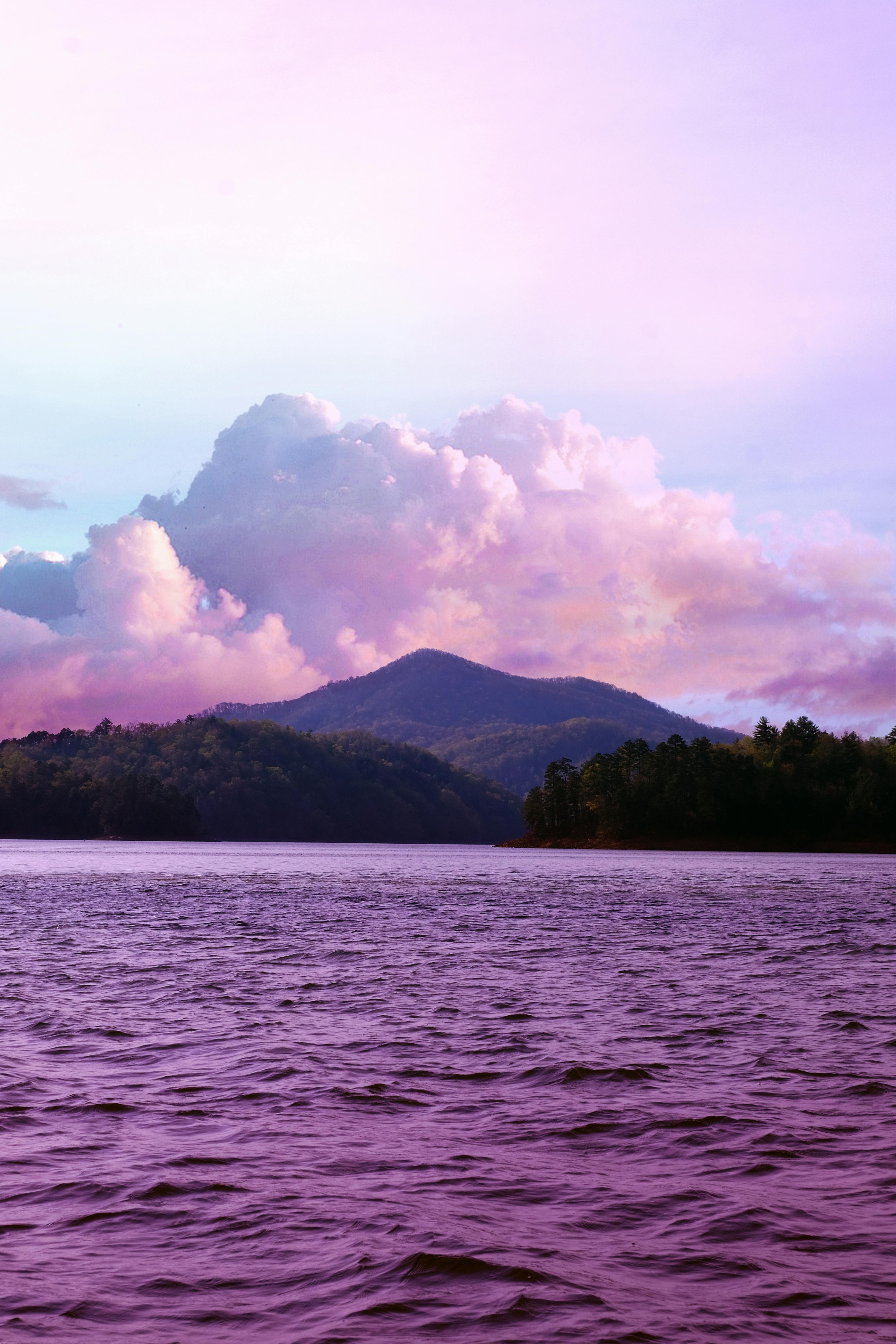 A serene pink-hued lake with distant hills under vibrant twilight clouds.