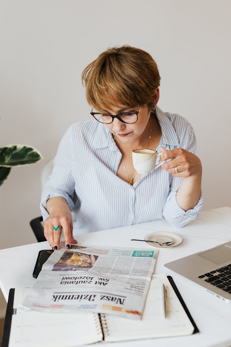 Serious Woman With Cup Of Coffee Reading Newspaper