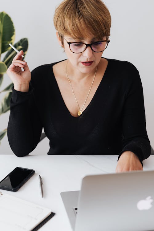 High angle of concentrated short haired businesswoman in eyeglasses smoking cigarette while working on laptop in modern office