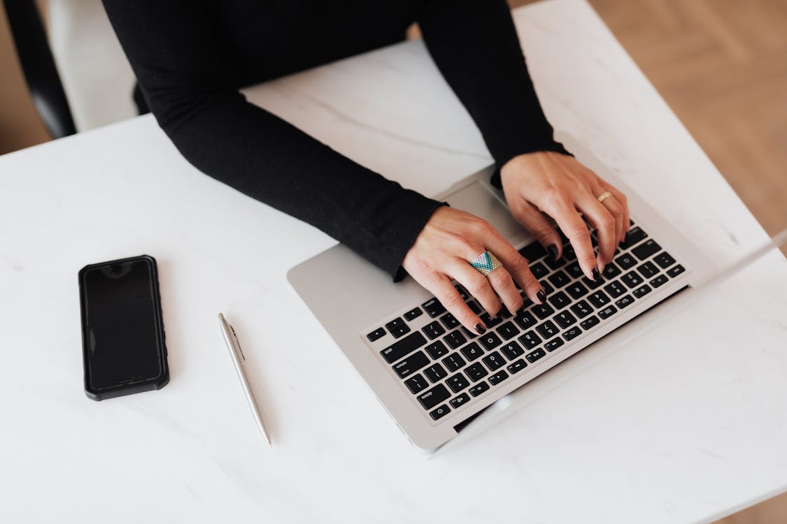 Free From above of crop anonymous young female programmer typing on netbook keyboard while sitting at table with smartphone in modern workspace Stock Photo