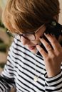 Crop short haired female entrepreneur in casual clothes and eyeglasses having phone conversation while working remotely