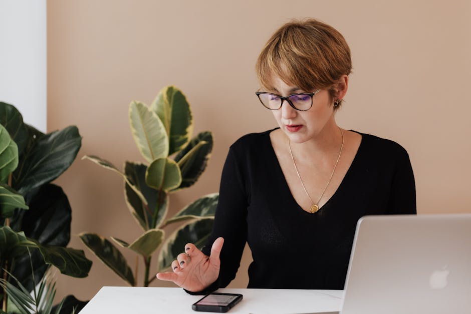 Concentrated female manager in casual outfit and eyeglasses reading message on smartphone while sitt