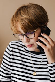 Focused middle aged female in striped sweater and eyeglasses having phone call while working distantly at home