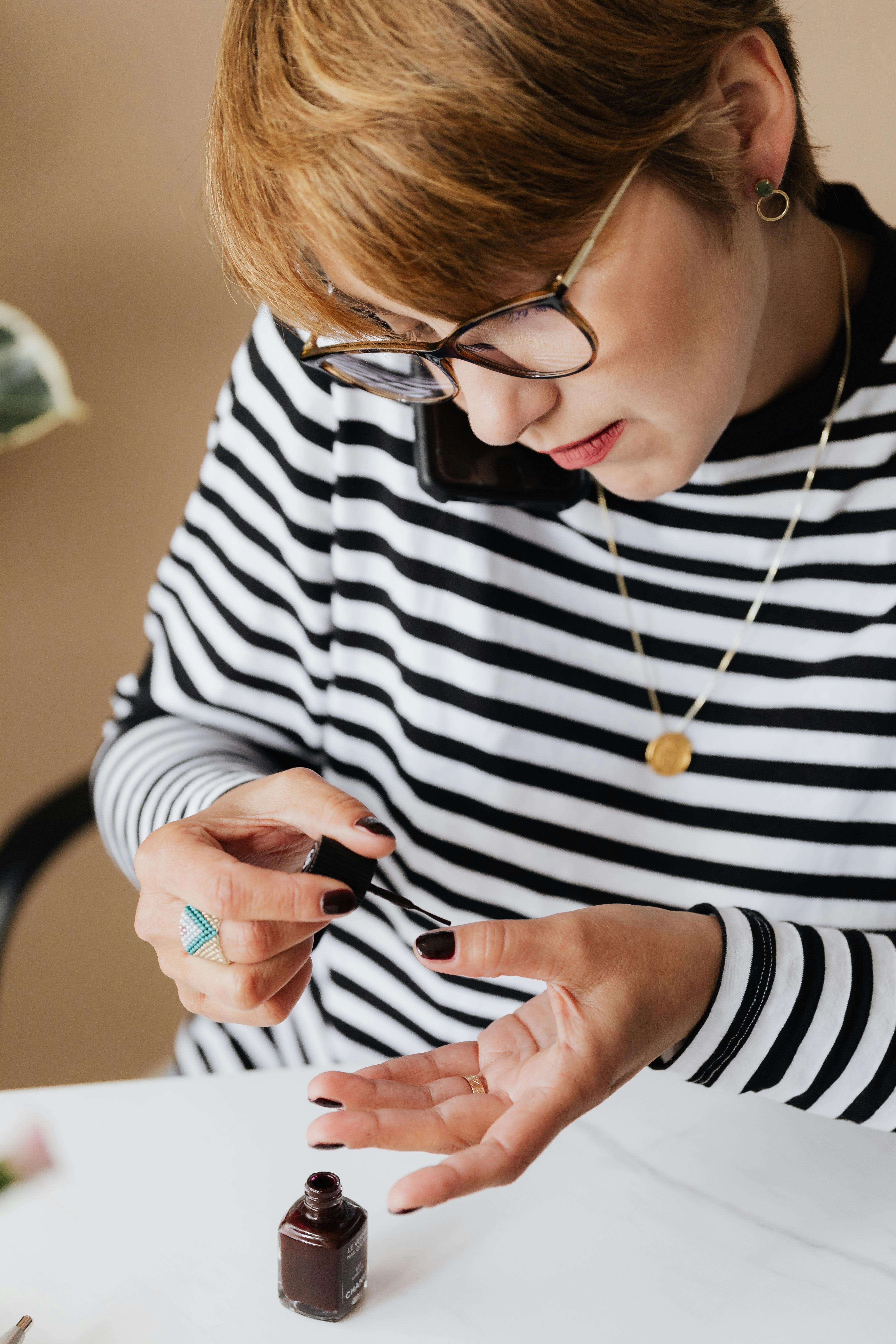 concentrated woman applying nail polish and talking on smartphone at home