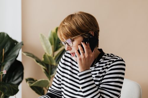 Free Busy short haired adult lady in eyeglasses sitting in comfortable armchair and talking on smartphone while working in modern office Stock Photo