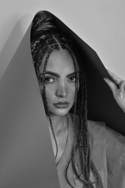 Black and white pretty female model with braids looking at camera and covering head with sheet of paper