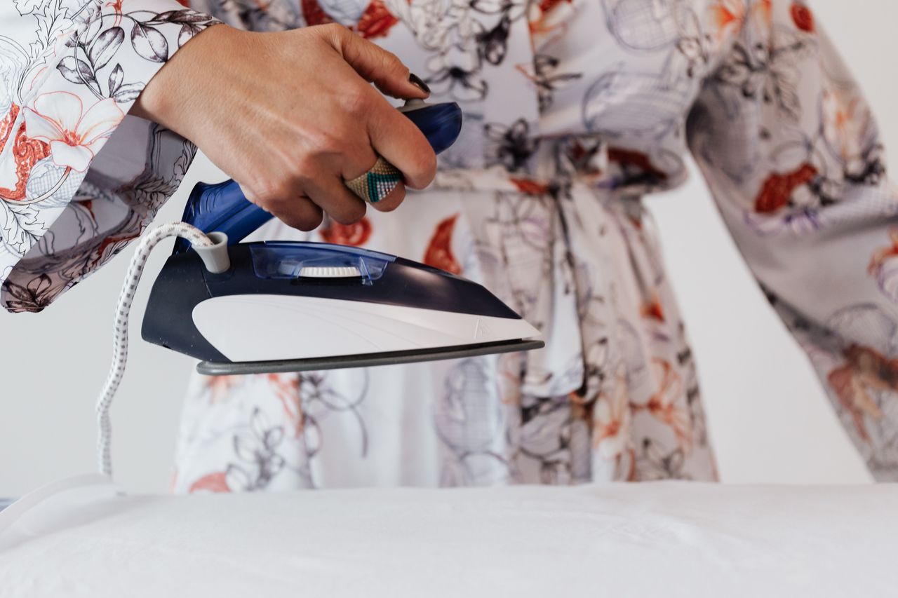 Hand lifting a steam iron over smooth white fabric on an ironing board